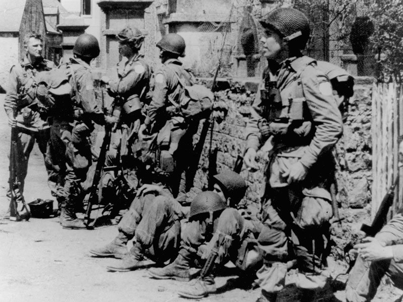 A black and white photograph of several Soldiers standing and sitting along a stone ledge.